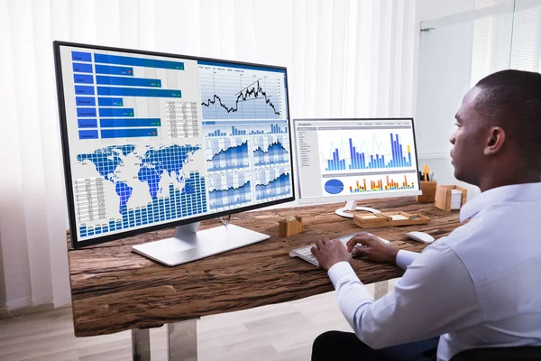 職場で木製の机の上のコンピューターでグラフを分析ビジネスマンの背面図 — ストック写真