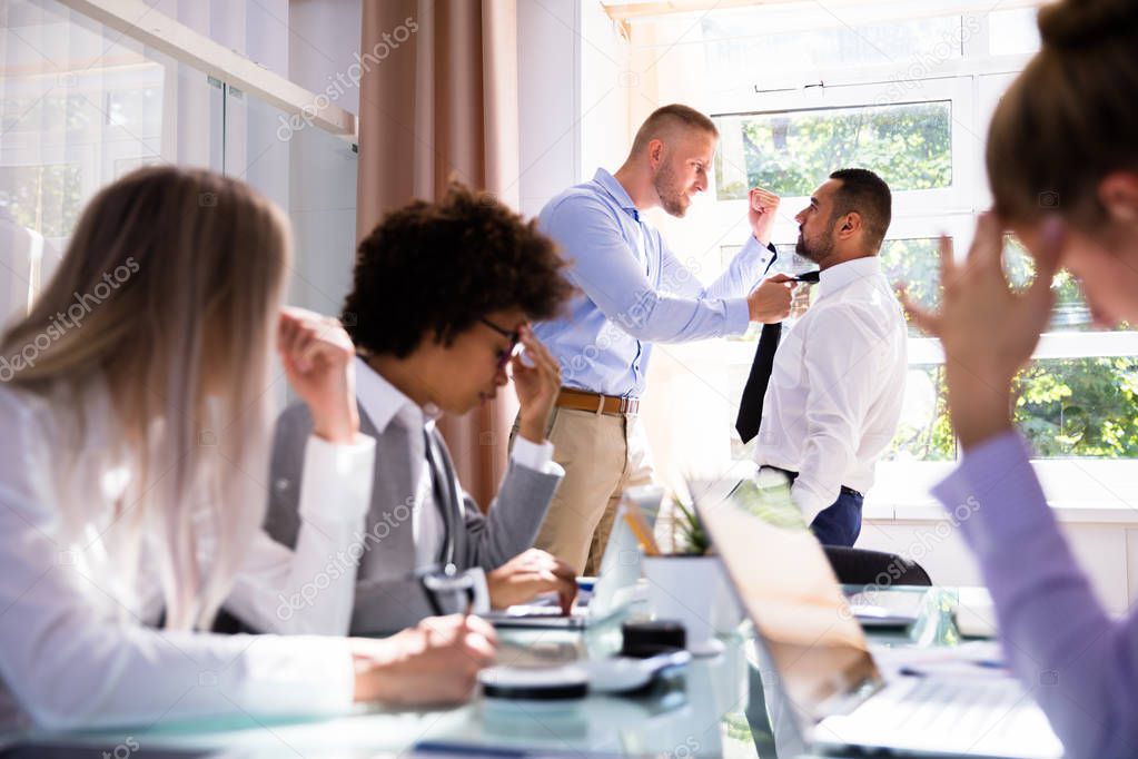 Stressed Businesspeople Sitting In Front Of Two Colleagues Fighting In Office