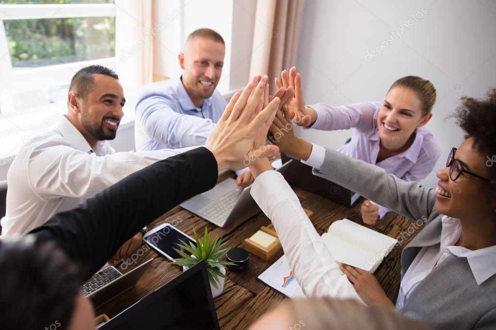 Group Of Happy Young Businesspeople Giving High Five In Office