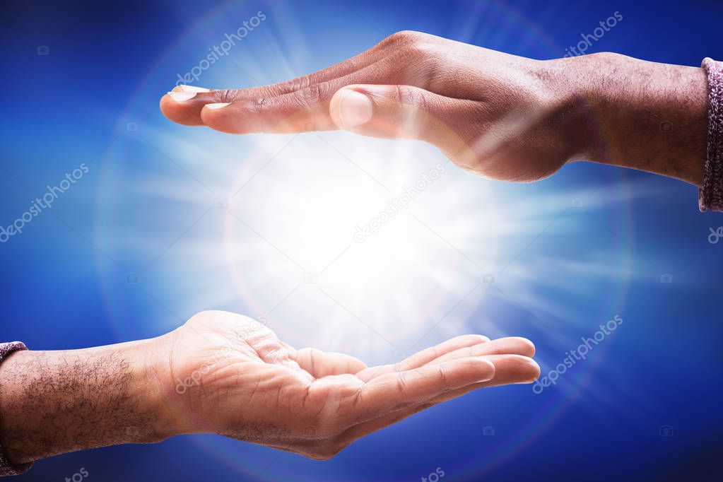 Male's Hand Collecting Glowing Sunlight Flare Against Blue Background