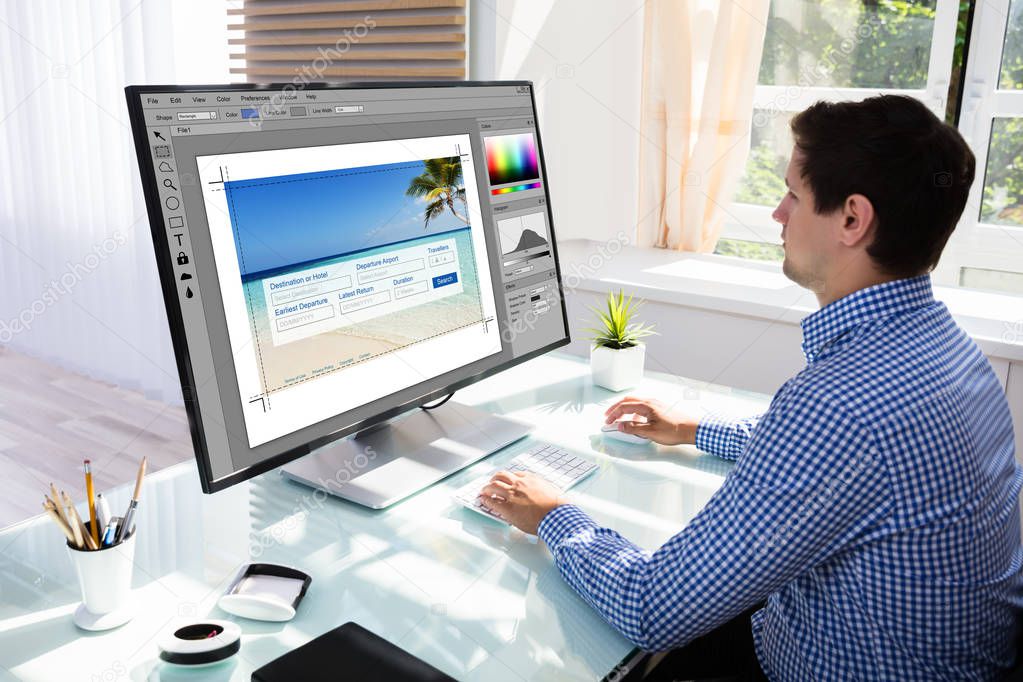 Young male designer editing photos on computer in office