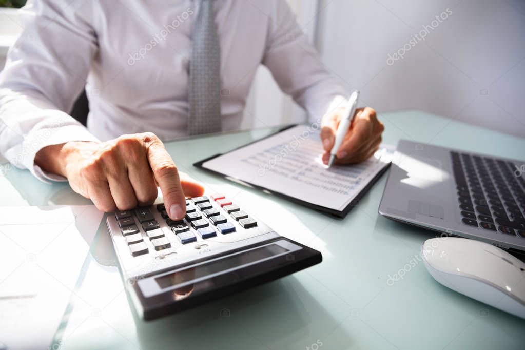 Close-up Of A Businessman's Hand Calculating Invoice With Calculator