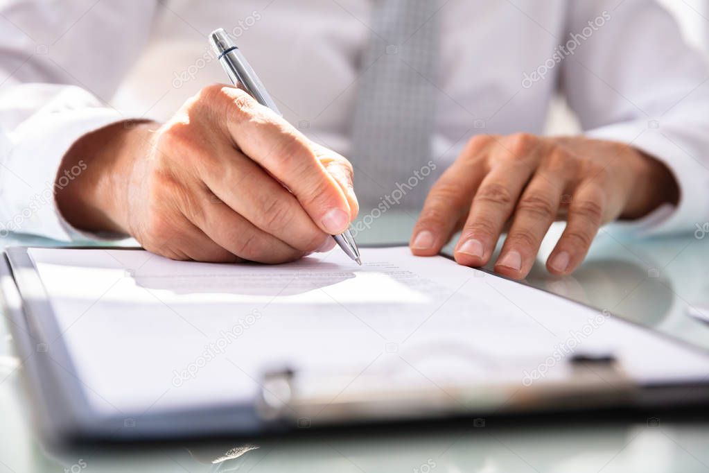 Businessman's Hand Filling Contract Form With Pen