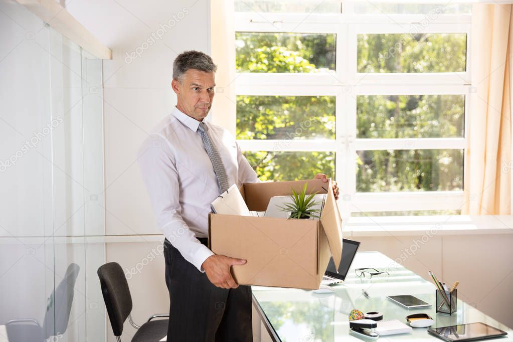 Unhappy Mature Businessman Carrying Belongings In Cardboard Box At Workplace