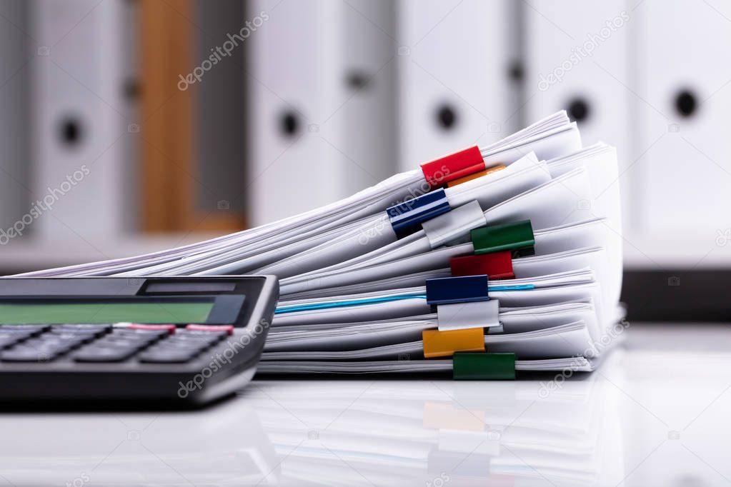 Close-up Of Calculator And Stacked Documents On Reflective Desk