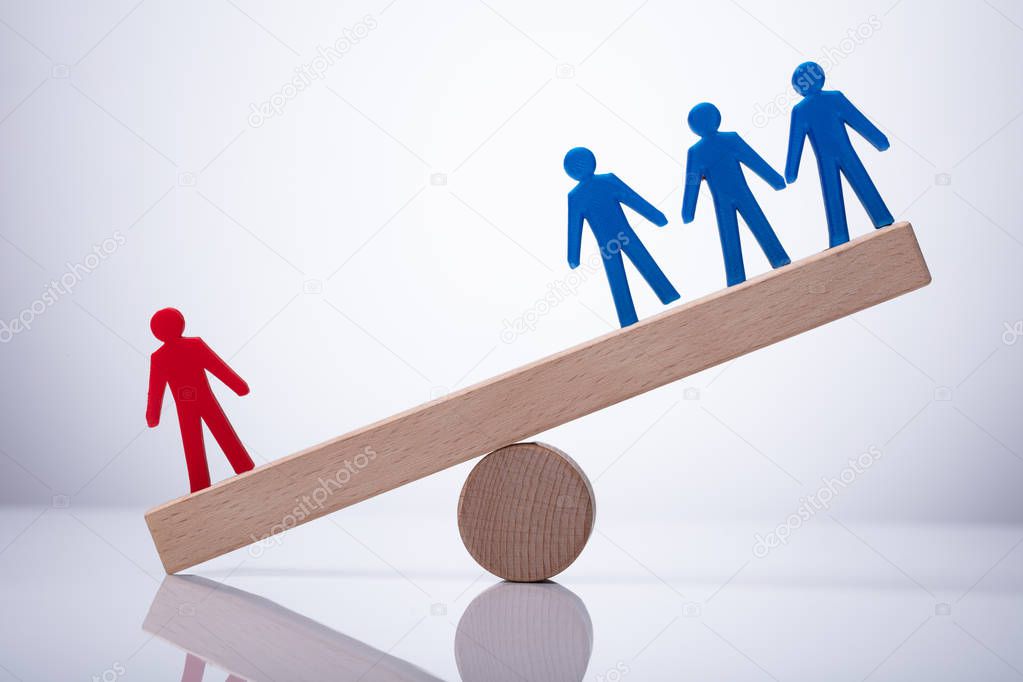 Red Human Figure Standing Against Blue Team On Wooden Seesaw