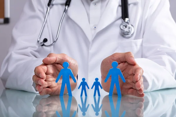 Doctor Hand Protecting Blue Family Figure Cutout Reflective Desk — Stock Photo, Image