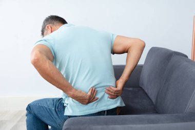 Sırt ağrısı muzdarip kanepede oturan olgun adam