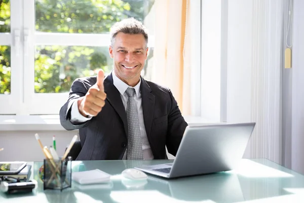 快乐的商人示意拇指与笔记本电脑在办公桌上 — 图库照片