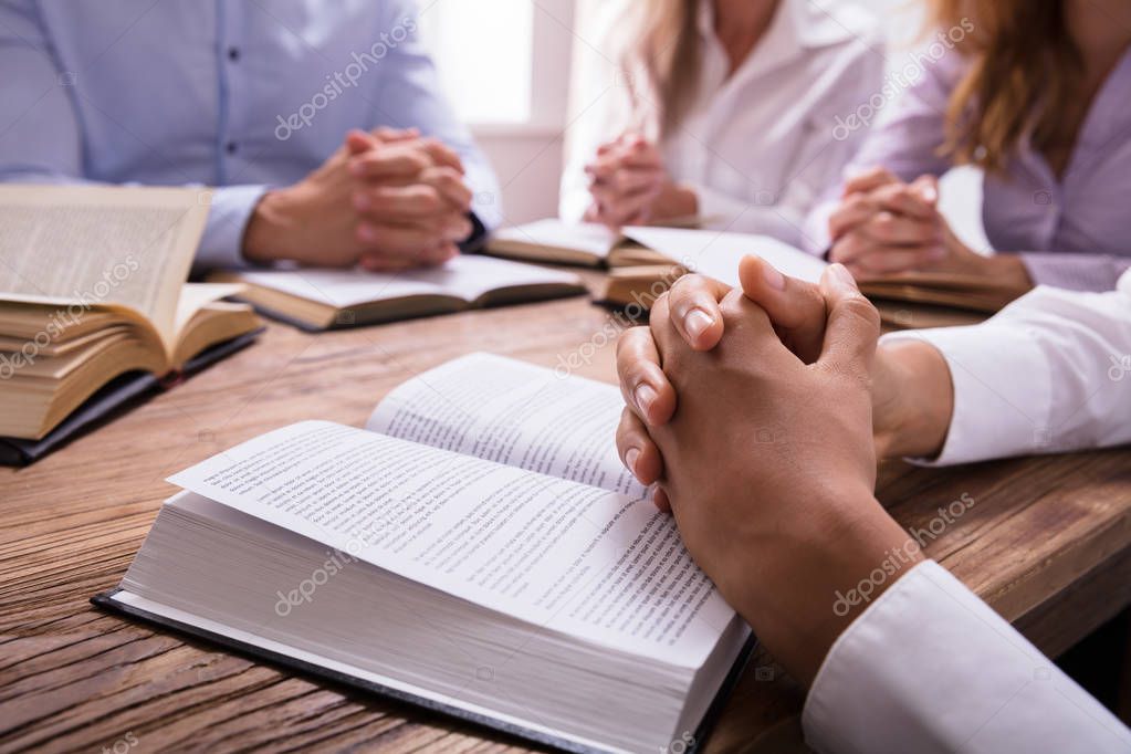 Close-up Of A Woman's Praying Hand On Bible Over Wooden Desk
