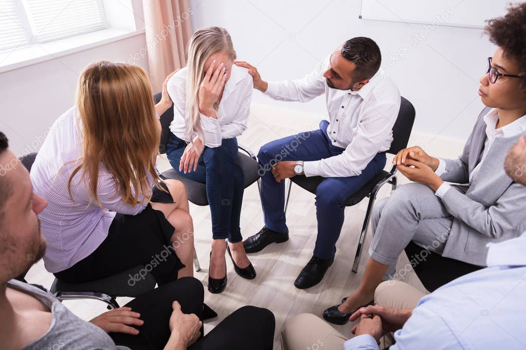 Group Of People Consoling Devastated Young Woman In Group Therapy Session