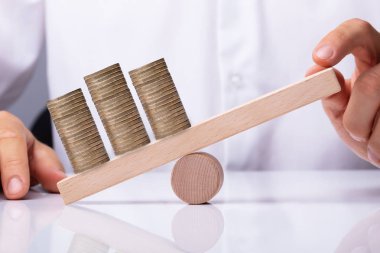 İnsan eli ahşap tahterevalli üzerinde yığılmış altın sikke Dengeleme