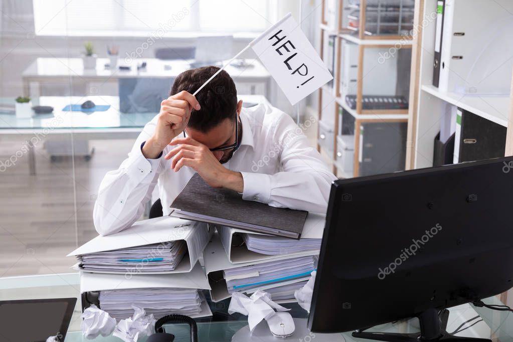 Overworked Businessman Holding Help Flag With Stack Of Folders On Desk