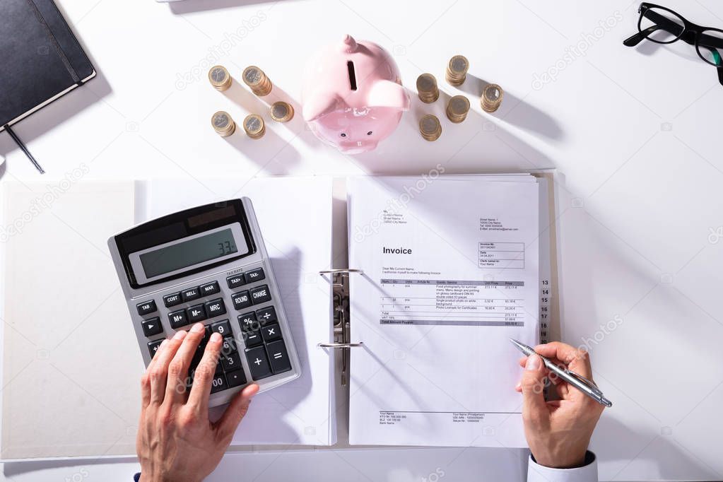 Elevated View Of Businessman Calculating Invoice With Piggybank And Coins On Desk