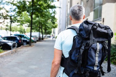 Bir adam kaldırımda yürüyen sırt çantası ile arkadan görünüş