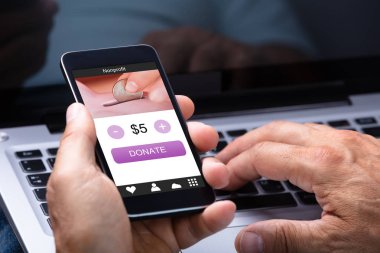 Dizüstü bilgisayar kullanarak ve cep telefonu ile bağış App ekranda tutan adam