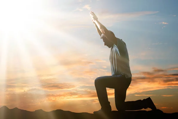 在日落时分 一个人跪着对着多云的天空祈祷的侧面视图 — 图库照片