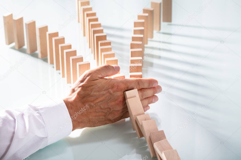 Close-up Of Businessman's Hand Stopping Wooden Blocks From Falling On Desk