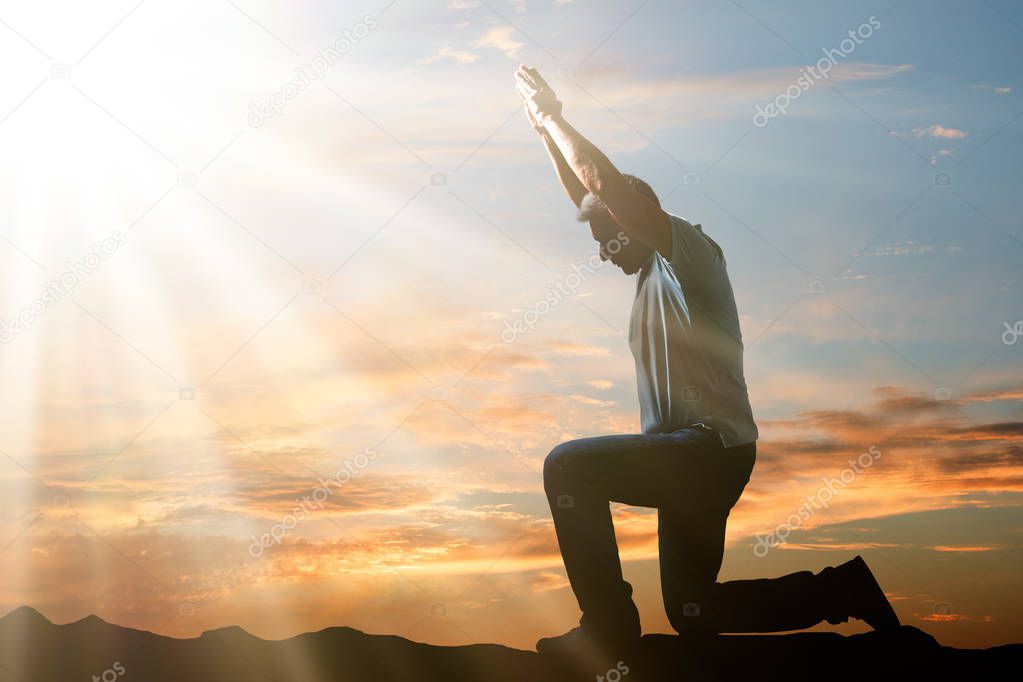 Side View Of A Man Kneeling And Praying Against Cloudy Sky At Sunset