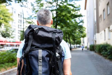 Bir adam kaldırımda yürüyen sırt çantası ile arkadan görünüş