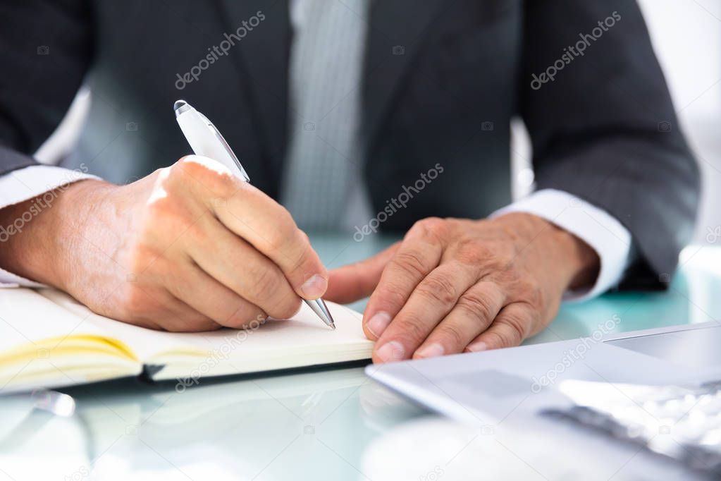 Businessman's Hand Writing Schedule In Diary With Pen