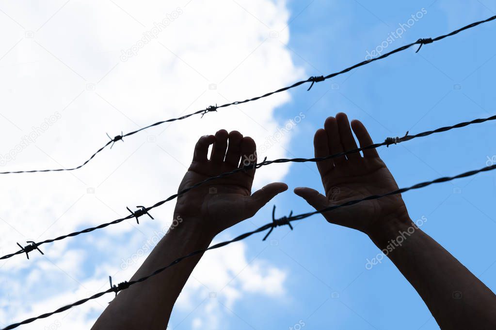Low Section View Of A Refugee Hand Holding Barbed Wire Fence