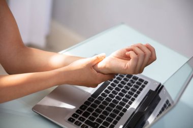 Dizüstü bilgisayar ile ağrılı bilek masanın üzerinde tutarak işkadını