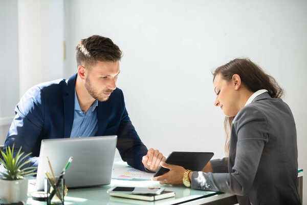 Two Young Businesspeople Using Digital Tablet At Workplace