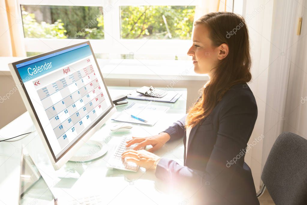Young Businesswoman Looking At Calendar On Computer Screen Over Desk