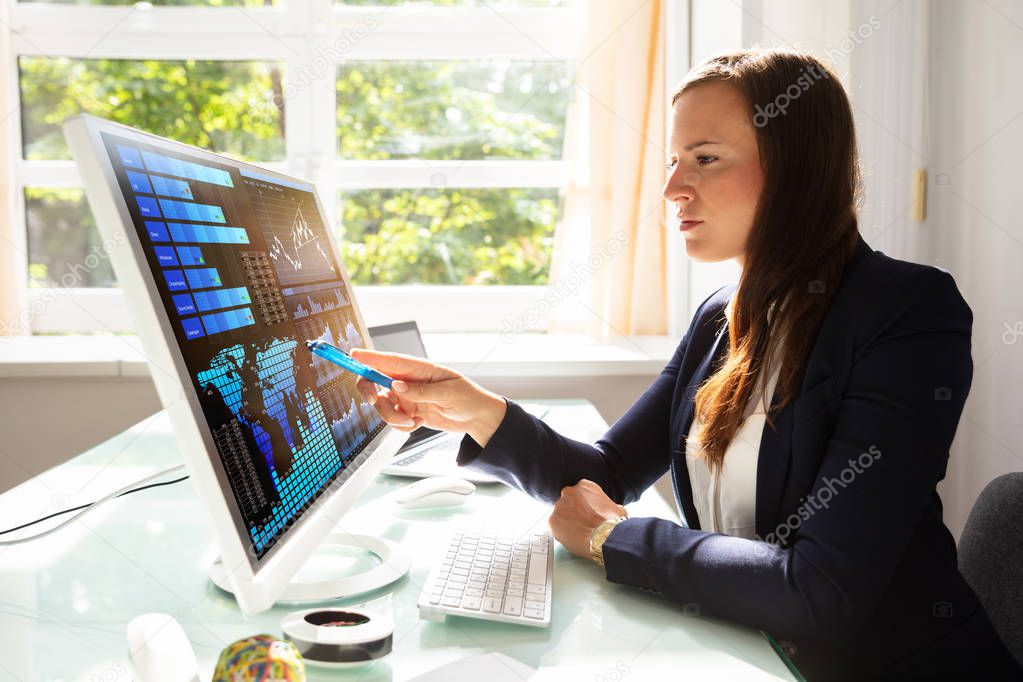 Young Businesswoman Analyzing Graphs On Computer At Workplace