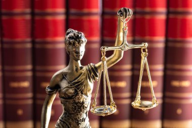 Altın renkli adalet heykeli önünde kırmızı hukuk kitapları