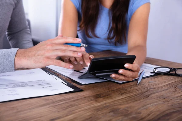 Close-up Of A Couple Calculating Invoice With Calculator Over Wooden Desk