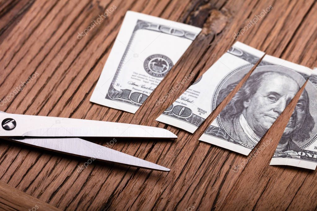 Cutted Dollar Banknote And Scissor On Wooden Table