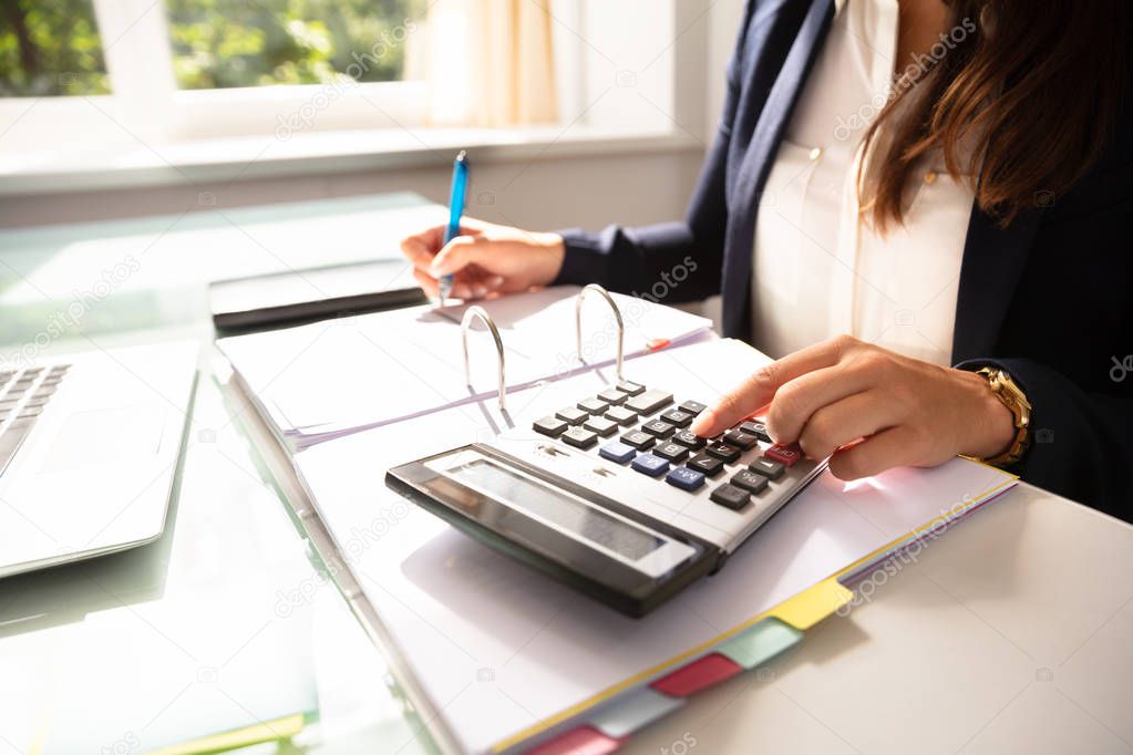 Businesswoman's Hand Calculating Invoice With Calculator In Office