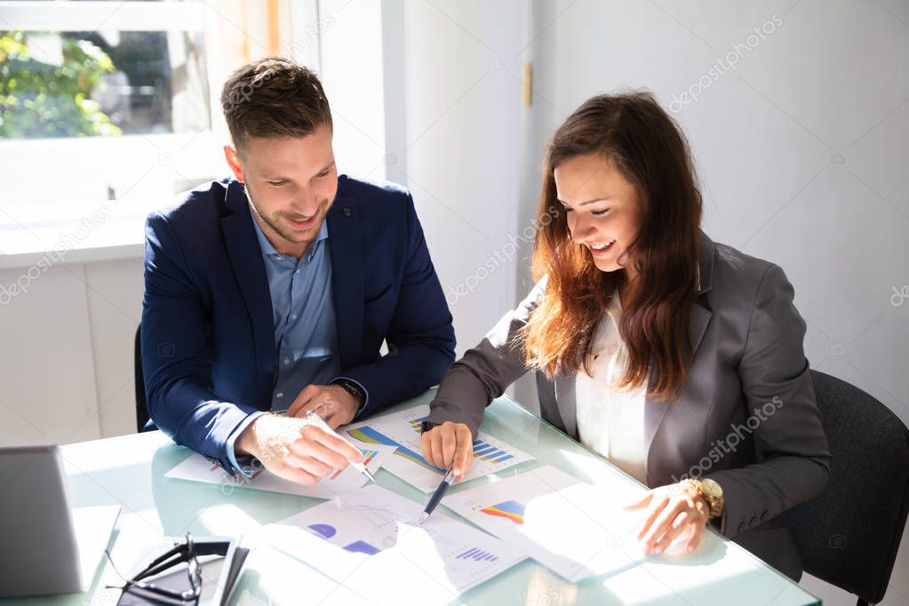 Two Young Businesspeople Analyzing Graph Over Office Desk