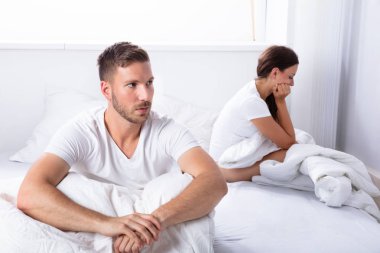 Mutsuz genç çift yatak yatak odasında oturup...