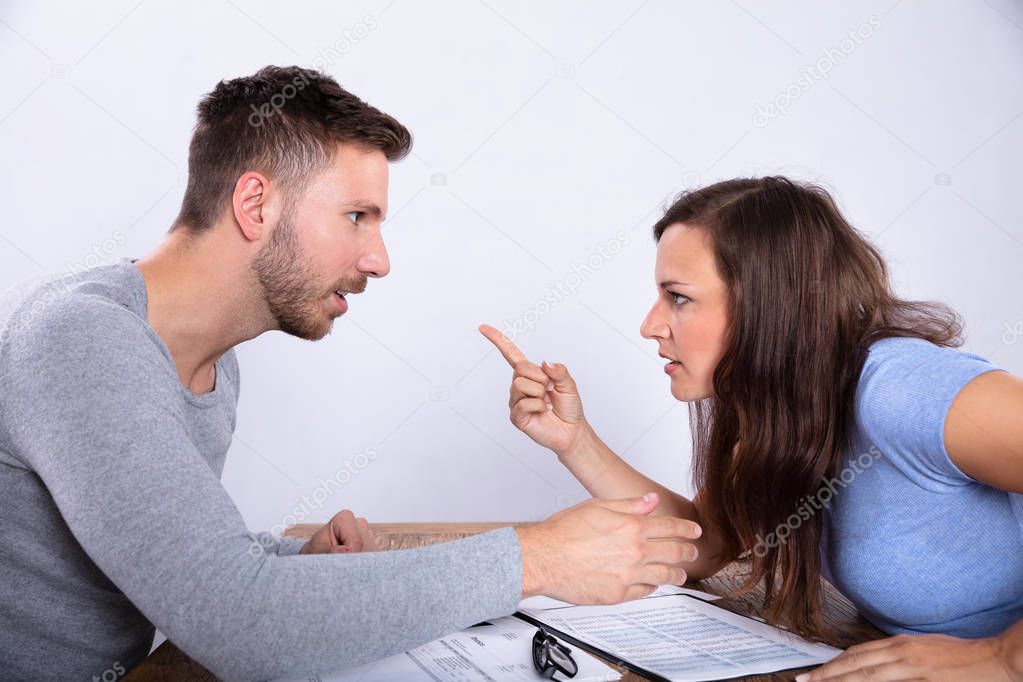 Young Couple Blaming Each Other With Documents On Wooden Desk