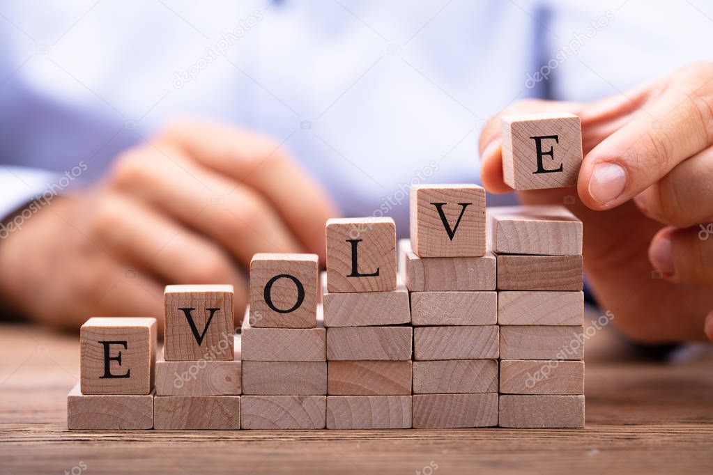 Close-up Of Person's Hand Placing Last Alphabet Of Word Evolve On Wooden Block