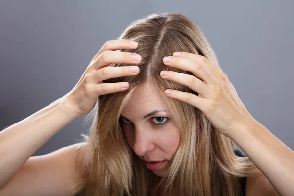 Ξανθιά Νεαρή Γυναίκα Που Εξετάζει Μαλλιά Πάνω Από Γκρίζο Φόντο — Φωτογραφία Αρχείου