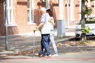 Genç bir kadın yoldan geçerken babasına yardımcı yan görünüm