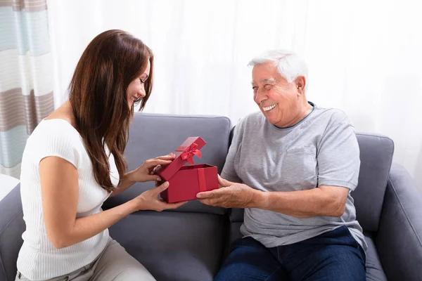 Woman Giving Gift Her Happy Father Sitting Sofa — Stock Photo, Image