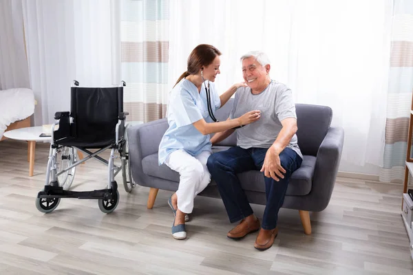 Kvinna Sjuksköterska Kontrollera Lycklig Senior Man Sitter Soffan Med Stetoskop — Stockfoto