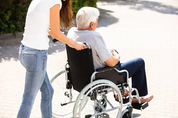 帮助残疾父亲的年轻妇女在轮椅在室外 — 图库照片