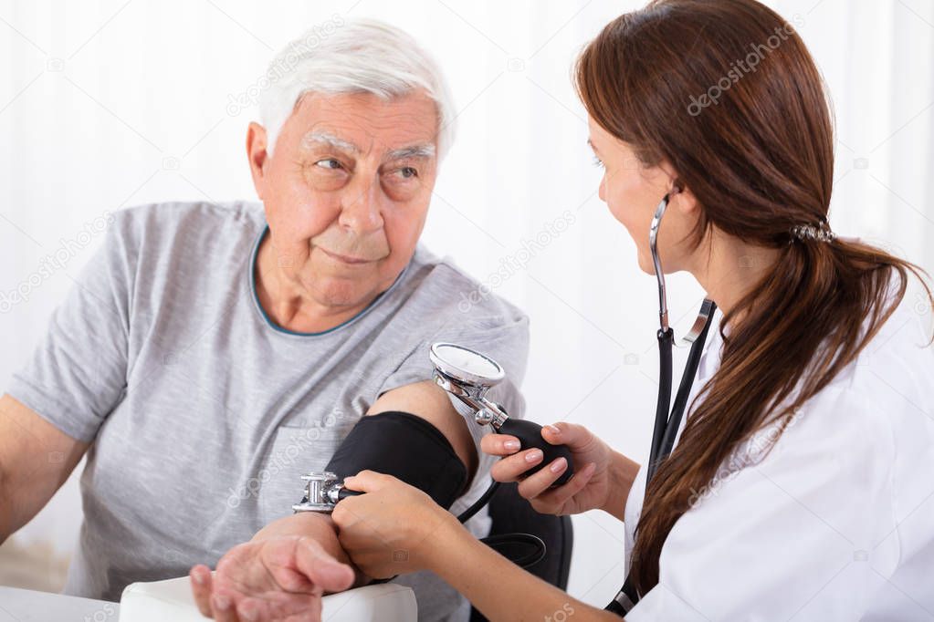 Young Female Doctor Checking Blood Pressure Of Senior Male Patient In Clinic