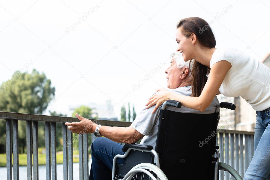 Young Woman With Her Disabled Father Near Railing At Outdoors