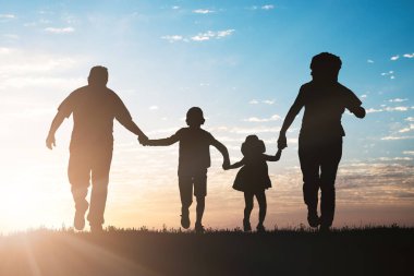 Gökyüzü karşı parkta günbatımında çalışan aile silüeti