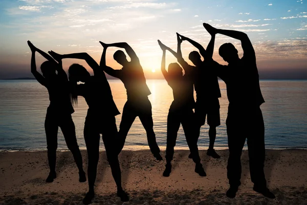 Silhouette Of People Doing Yoga In Park At Sunset