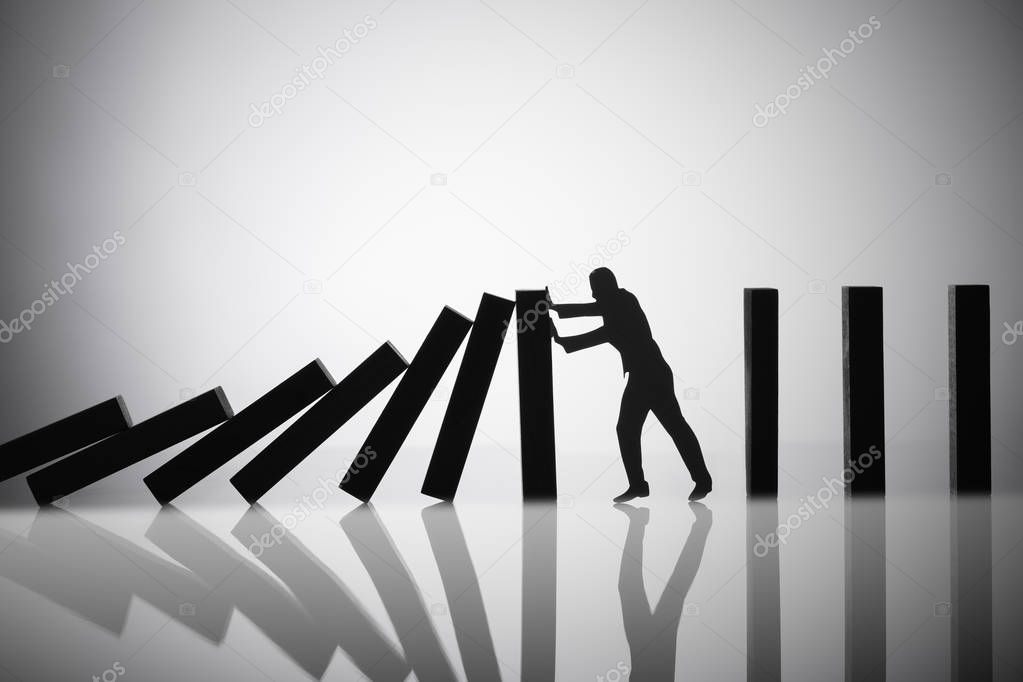 Silhouette Of A Person Stopping Falling Dominoes On Reflective Background