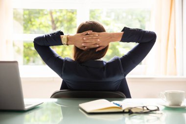 Ofiste oturan başının arkasında elleriyle rahat iş kadını