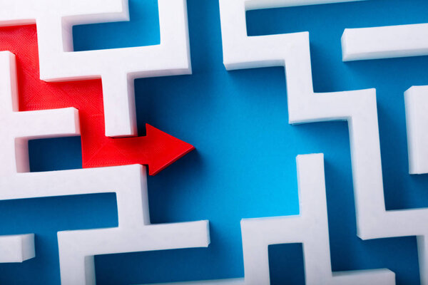Elevated View Of Red Arrow At The Center of White Maze On Blue Surface
